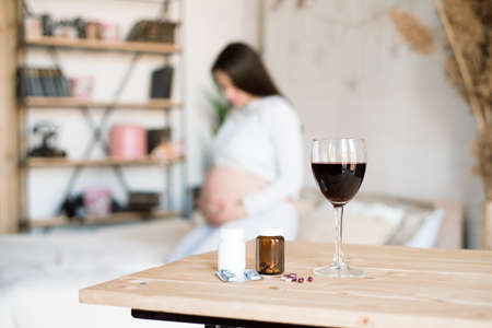 A glass of red wine and pills on the background of a pregnant woman. Alcoholic concept.の写真素材