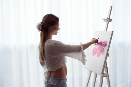 Portrait of a young pragnant woman painting with oil paints on white canvas, side view portraitの写真素材