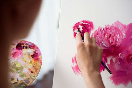 Painter drawing in art studio using easel. Portrait of a young woman painting with oil paints on white canvas, side view portraitの写真素材