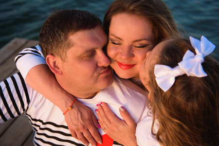 a pregnant mother, her husbant and daughter relaxing on the bridge by the river
