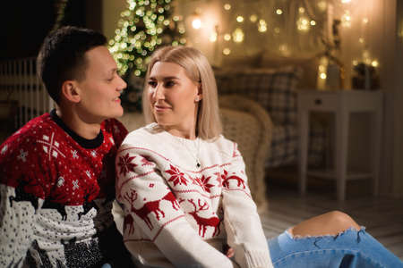 Couple in knit sweaters near Christmas tree. Man and woman in Christmas interior room.の写真素材