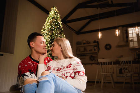Lovely couple sitting on carpet wearing christmas sweater and hugging.の写真素材