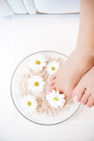Female feet with spa bowl, towel and flowers on white backgroundの写真素材