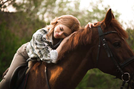 Woman with long hair posing with a brown horse in a forest in a sunny meadow.の写真素材