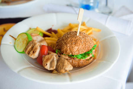 Wedding banquet in a restaurant, party in a restaurant, burger and chicken skewers in a white plate.