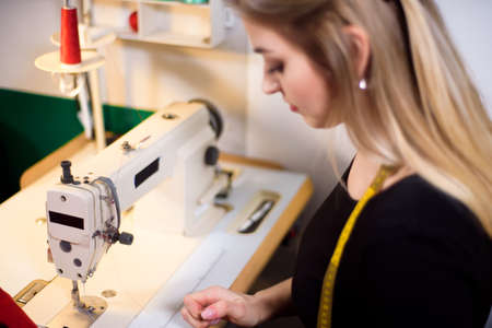 Tailor laboring at working place in atelier. Sewing machine, ruler, scissors, table lamp, threads on background.の写真素材