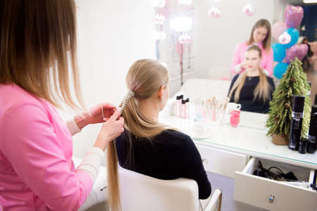 Female hairdresser makes a hairstyle to a blonde girl in a beauty salon.の写真素材