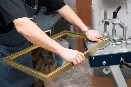 Craftsman working on frame in frameshop. Professional framer hand holding frame angle. Top view.