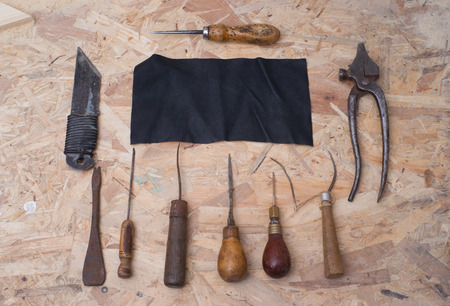 Leather craft tools on a wooden background. Craftmans work desk . Piece of hide and working handmade...