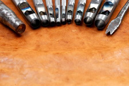 Leather craft tools on a wooden background. Craftmans work desk . Piece of hide and working handmade...