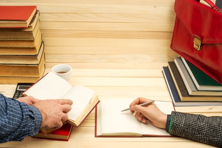 Financial concept. Business partners discuss profit and losses, analyzing financial results. On a wooden table books, documents, calculator, stapler, red briefcase.の写真素材