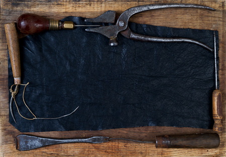 Leather craft tools on a wooden background. Craftmans work desk . Piece of hide and working handmade...
