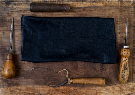 Leather craft tools on a wooden background. Craftmans work desk . Piece of hide and working handmade tools on a work table. Top view.の写真素材
