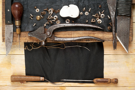 Leather craft tools on a wooden background. Craftmans work desk . Piece of hide and working handmade...