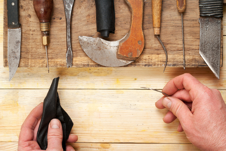 Leather craft tools on a wooden background. Craftmans working with leather using crafting DIY tools. Piece of hide and working  handmade tools on a work table. Top view.  Copy space.の写真素材