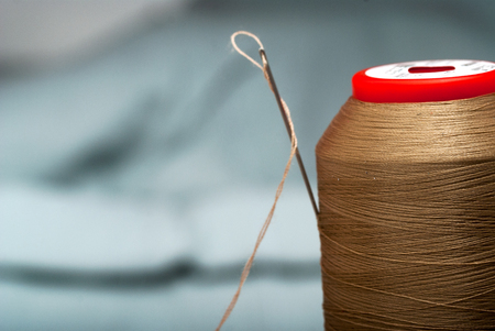 Sewing textile or cloth. Work table of a tailor. Detail of a needle with thread in the workroom reel of thread, and natural fabric. . Shallow depth of field. Focus on needle.の写真素材