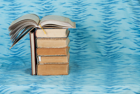 Open book, stack of hardback books  on blue cloth. Back to school. Copy space