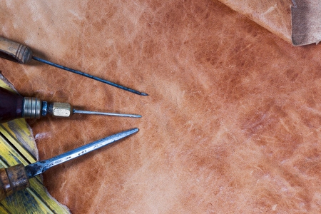 Leather craft tools on a wooden background. Leather craftmans work desk . Piece of hide and working...