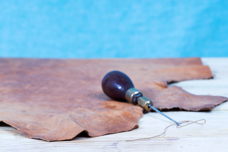 Leather craft tools on a wooden background. Leather craftmans work desk . Piece of hide and working...