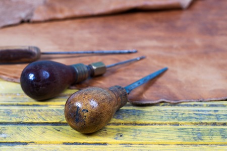 Leather craft tools on a wooden background. Leather craftmans work desk . Piece of hide and working handmade tools on a work table.の写真素材