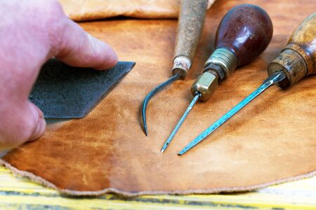 Leather craft tools on a wooden background. Leather craftmans work desk . Piece of hide and working...