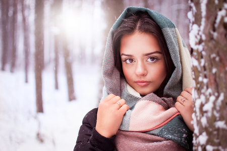 Beautiful brunette in a black jacket standing in a winter forestの写真素材