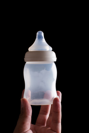 Man hand is handle empty baby bottle on black background.の写真素材