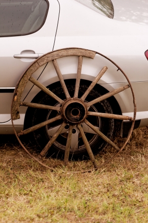 old broken wagon wheel side by new cars backの写真素材