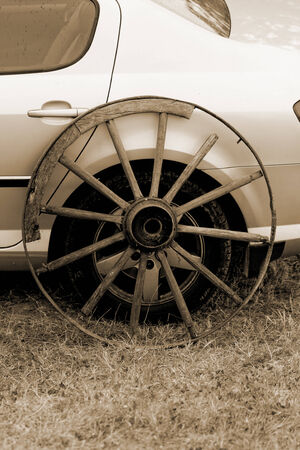 old broken wagon wheel side by new cars back sephiaの写真素材