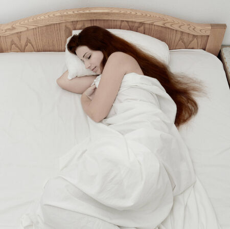 beautiful girl with long brown hair sleeping in the white bedの写真素材