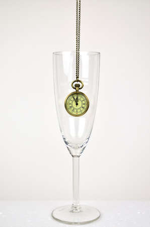 Hanging old watch in a glass of champagne for showing five minutes to twelve.