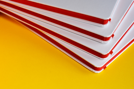 Four white notebooks with red paper on yellow backgroundの写真素材