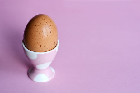 Boiled egg in pink egg holder with white polka dots on pink background