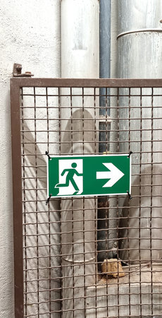 Metal fence with a green exit sign indicating the evacuation direction