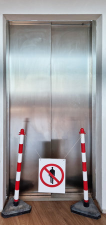 Metal elevator doors blocked by red and white poles and a no-access signの写真素材