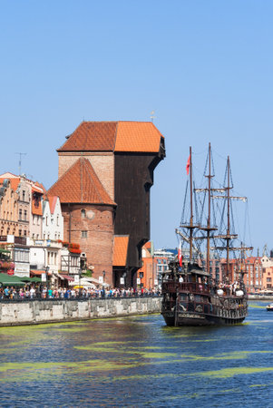 GDANSK, POLAND AUGUST 27, 2016: Old city with medieval wooden port crane, the oldest in Europe, Motlava river, tourist pirate ship and crowd of people walking along the quayのeditorial素材