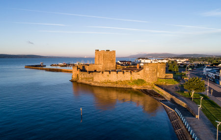 Medieval Norman Castle in Carrickfergus near Belfast, Northern Ireland. Aerial view at sunrise with far view of Belfast in the background.のeditorial素材