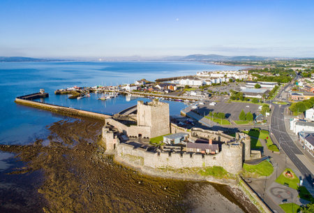 Medieval Norman Castle in Carrickfergus near Belfast in sunrise light. Aerial view with marina, yachts, parking, town and far view of Belfast in the background.のeditorial素材