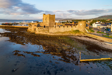 Medieval Norman Castle in Carrickfergus near Belfast in sunrise light. Aerial view with marina, yachts, parking, breakwater, groin, sediments and far view of Belfast in the backgroundのeditorial素材