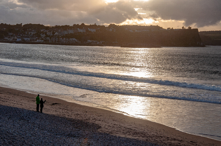 Ballycastle, Northern Ireland, UK. Atlantic coast. Beach, waves and unrecognizable pair in sunset light reflection with dark heavy cloudsの写真素材