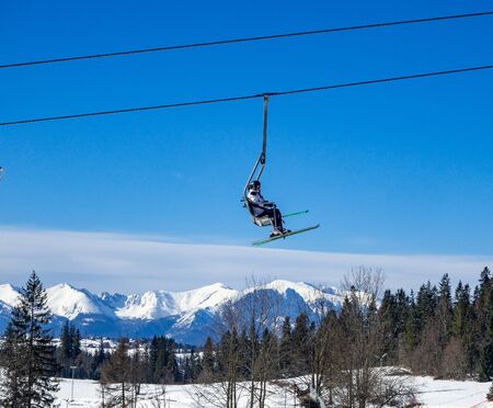 A chairlift with an unrecognizable skier on blue sky over Tatra mountains and a forest in Bialka ski resort in Polandの写真素材