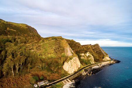 Northern Ireland, UK. Atlantic coast. Cliffs and Antrim Coast Road, a.k.a. Causeway Coastal Route. One of the most scenic coastal roads in Europe. Aerial view near Garron Point in sunrise lightの写真素材