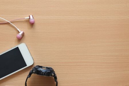 Top view of headphones and phone on wooden background.