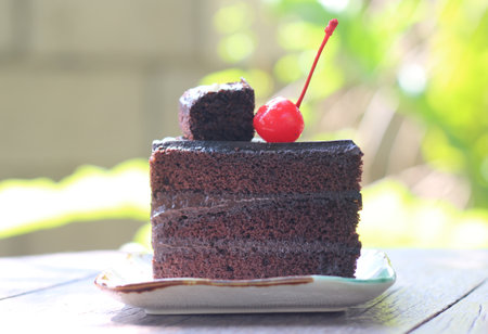 Chocolate cake with cherry on top on wooden table in garden.の写真素材