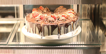 Chocolate cake with strawberries on a glass shelf in a shop.