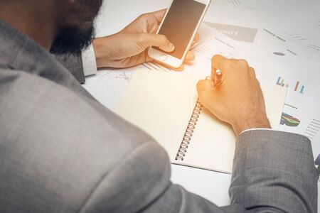 businessman write a note in paper while carry mobile phoneの写真素材
