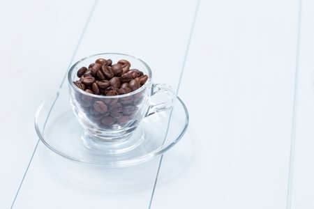 Coffee cup full of coffee beans on a wood tableの写真素材