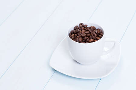 Coffee cup full of coffee beans on a wood tableの写真素材