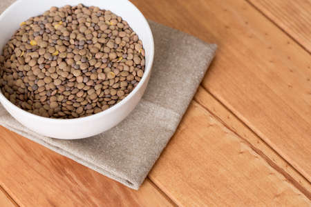 White bowl full of uncooked lentils on wooden tableの写真素材
