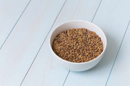 White bowl full of uncooked lentils on blue wooden tableの写真素材